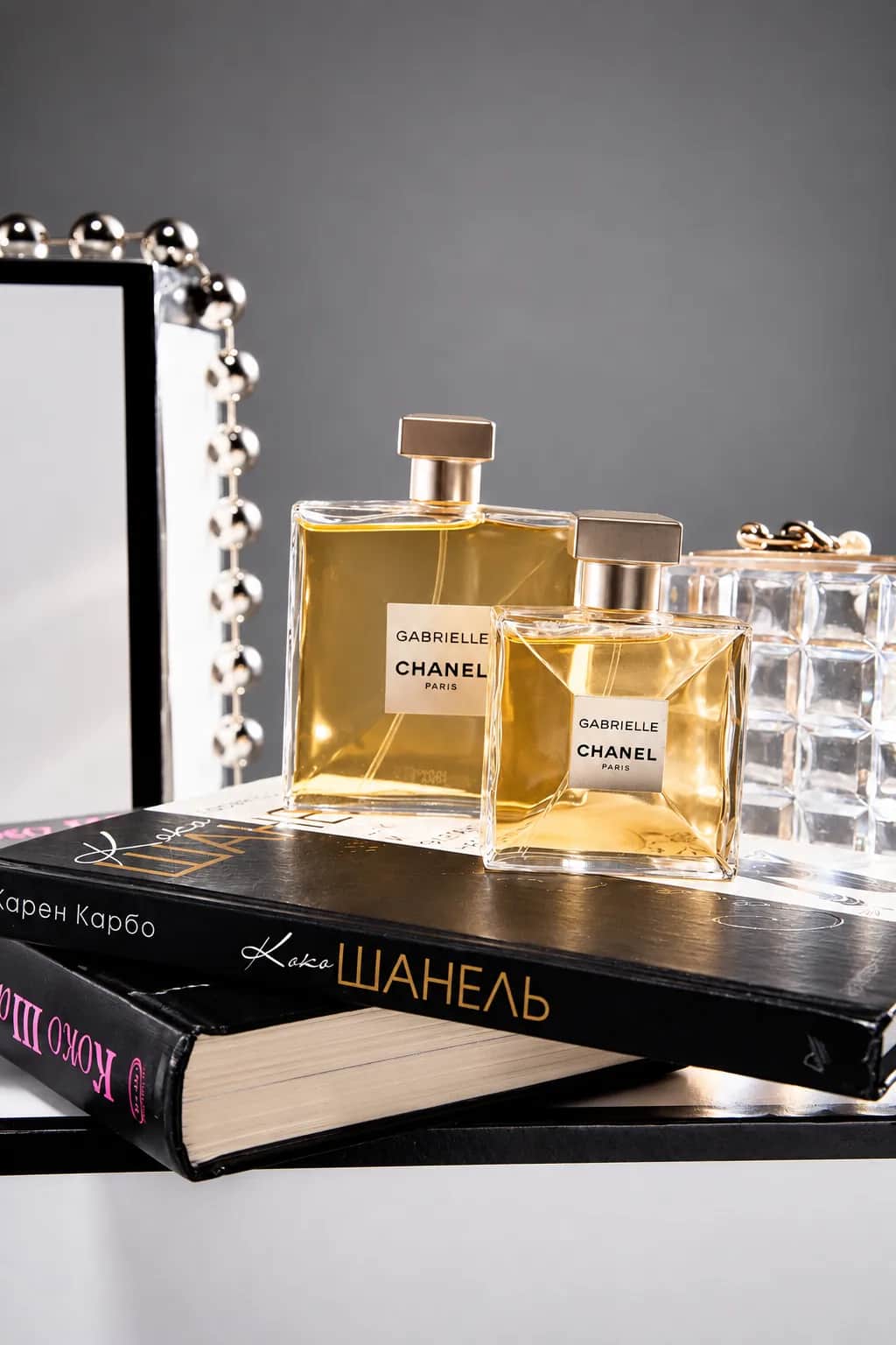 Флаконы Gabrielle Chanel на книгах рядом с прозрачным клатчем