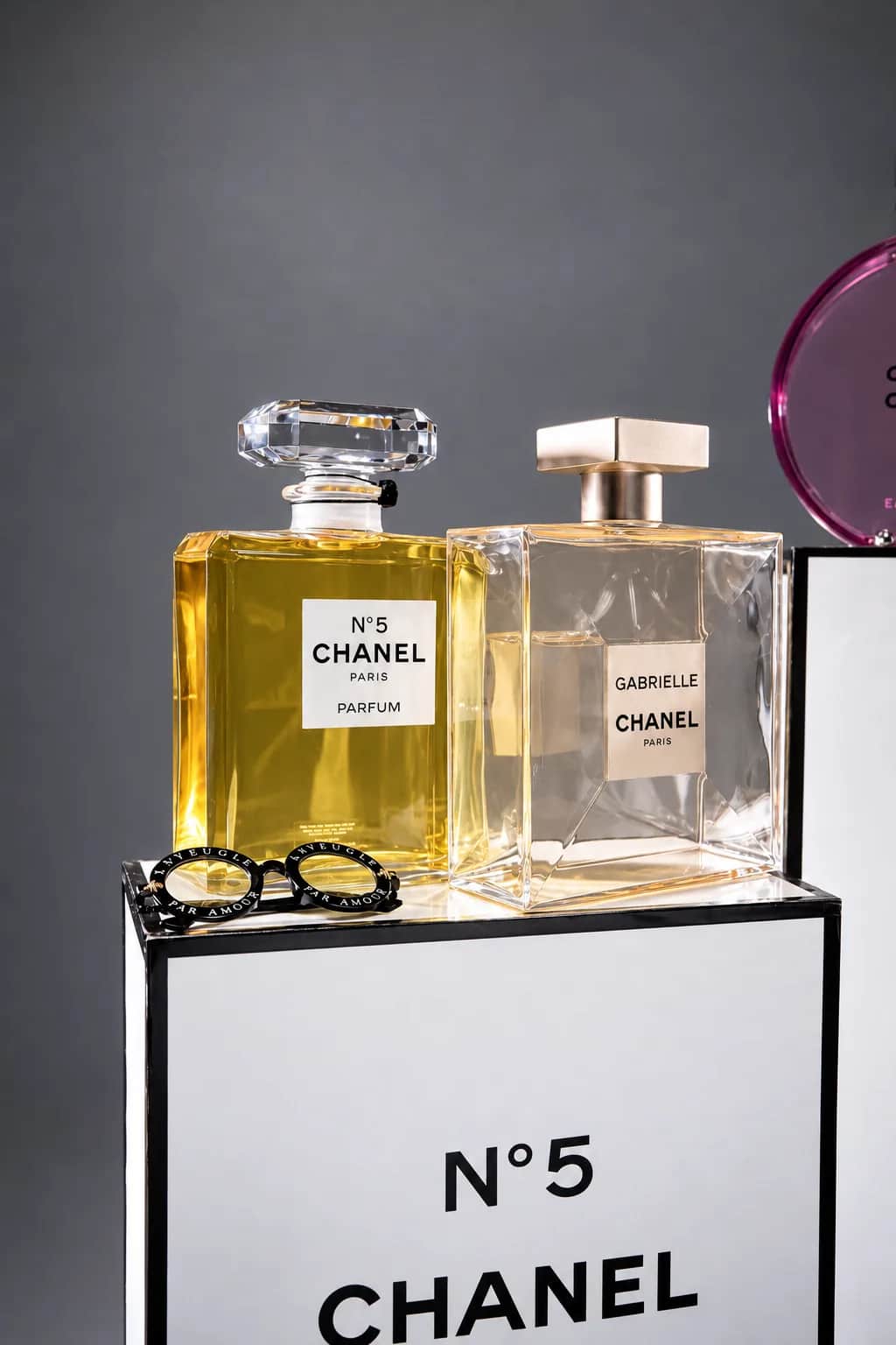 Декоративные флаконы Chanel N°5 и Gabrielle с очками на белом подиуме