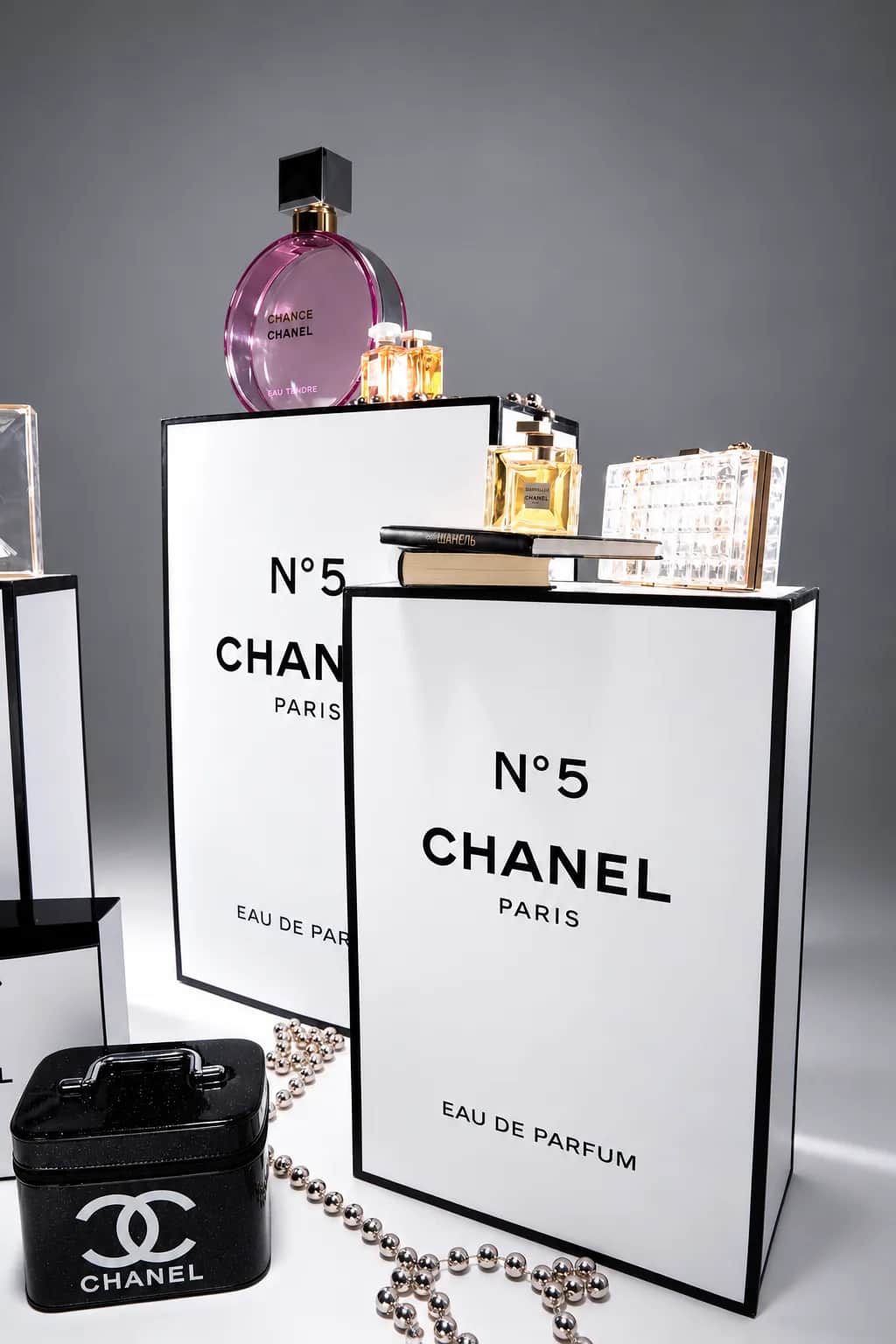 Белые подиумы CHANEL с флаконами, книгами и чёрным кейсом